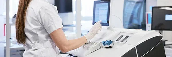 Medical professional operating an ABL800 FLEX PLUS blood gas analyzer in a clinical laboratory setting